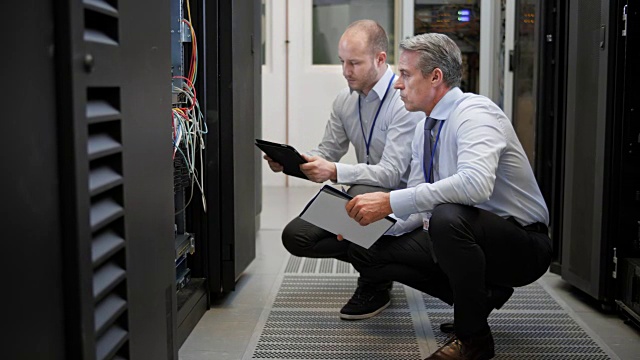两个技术人员蹲在服务器室讨论连接问题视频素材