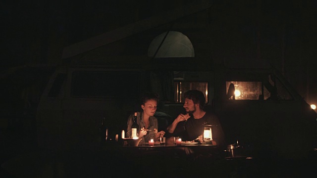 在法国南部的露营地，一对相爱的年轻情侣在烛光下坐在大众汽车前的露营桌旁吃意大利面。视频素材