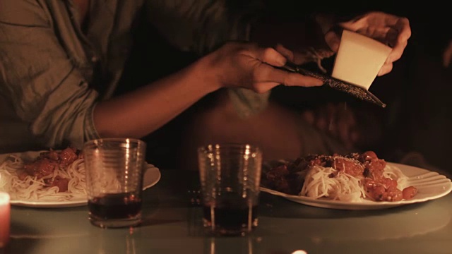 在法国南部的露营地，一名年轻女子在烛光下将帕尔马干酪放在意大利面上。视频素材