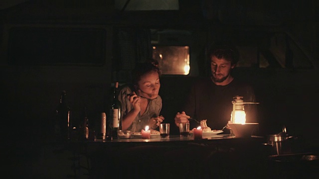 在法国南部的露营地，一对年轻情侣在大众汽车前的烛光下吃晚餐。视频素材