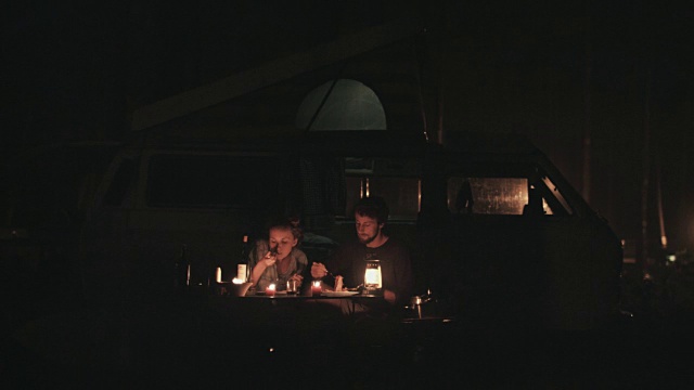 在法国南部的露营地里，一对年轻情侣坐在大众汽车前，在烛光下吃意大利面，笑着，谈笑风生。视频素材