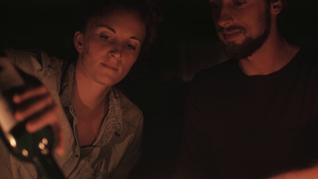 在法国南部的一个露营地，一对相爱的年轻情侣在烛光下在大众汽车前斟酒。视频素材
