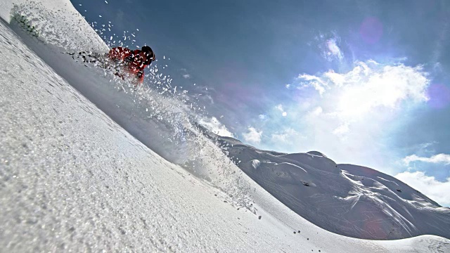 SLO MO滑雪板在一个阳光明媚的日子骑下山的粉末雪视频素材