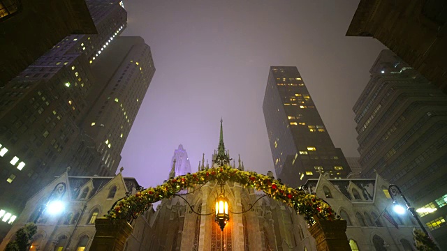 在曼哈顿中城的圣帕特里克大教堂和摩天大楼的雪夜。前面的大门是在纽约皇宫酒店，它被圣诞节装饰。视频下载