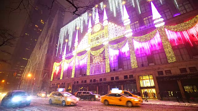 2016年曼哈顿中城的雪夜萨克斯第五大道假日灯光秀。萨克斯第五大道精品百货店的外部和橱窗都被装饰成圣诞装饰。汽车在白雪覆盖的第五大道上行驶。视频下载
