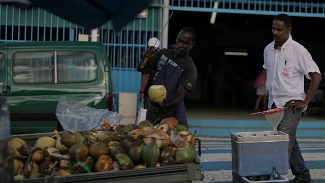 在马提尼克岛的当地市场上，一名非洲裔加勒比商人在卖椰子汁和喝椰子视频下载