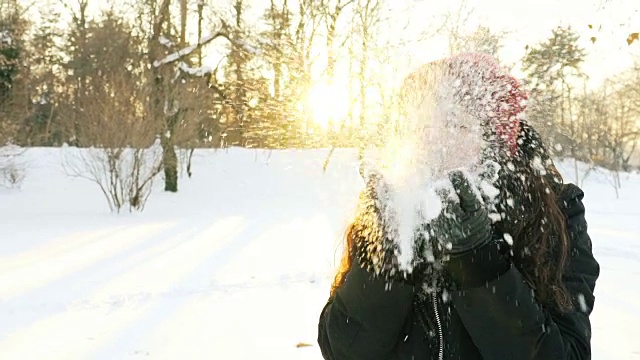 超级慢镜头:一名年轻女子在阳光明媚的冬日里吹着雪花。视频下载