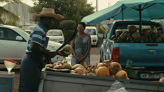 在马提尼克岛的当地市场上，一名非洲裔加勒比商人在卖椰子汁和喝椰子视频下载