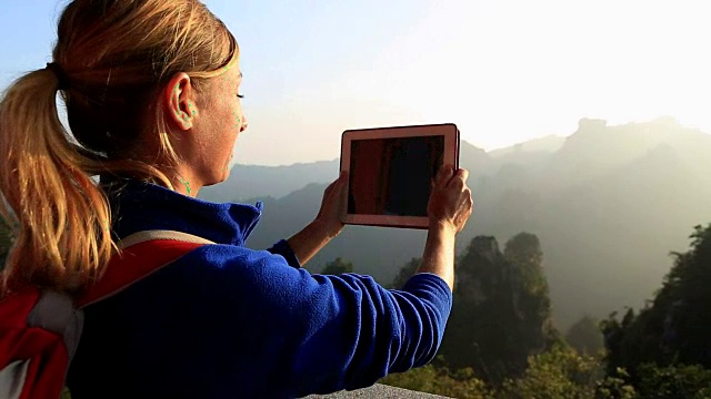 一名女性登山者在山顶用平板电脑拍照视频素材