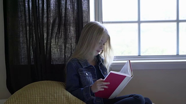 一个年轻的女孩在窗边看书。视频下载