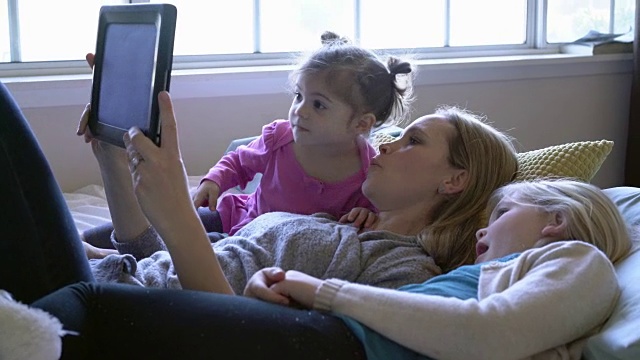 母亲在床上用平板电脑给女儿读书视频素材