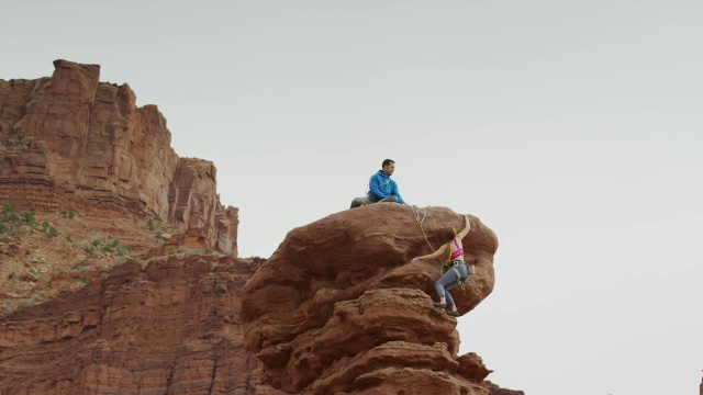 宽低角度平移拍摄夫妇攀登岩层/费舍尔塔，犹他州，美国视频素材