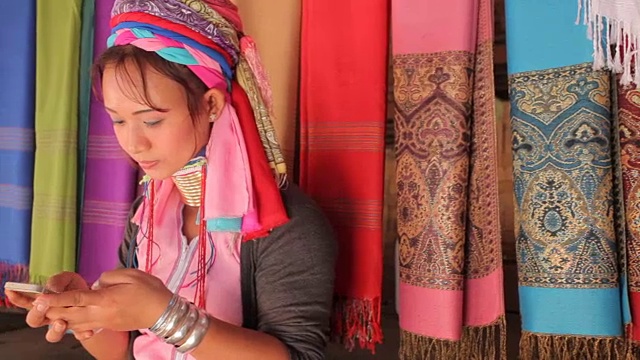 一名妇女穿着传统服装，拿着手机在村里织布视频下载