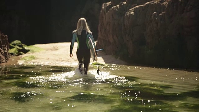 女冲浪者走过岩石池视频素材