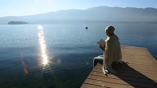 年轻女子坐在湖边的防波堤上读书视频素材
