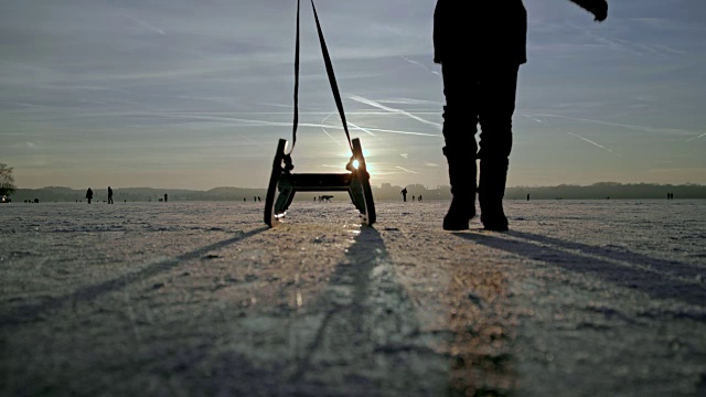 一个9岁的小男孩在结冰的湖面上拉着雪橇，边跑边看日落视频素材