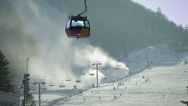 平昌(2018年冬奥会)滑雪场，人们在雪地上和空中缆车上玩滑雪板和滑雪。视频下载
