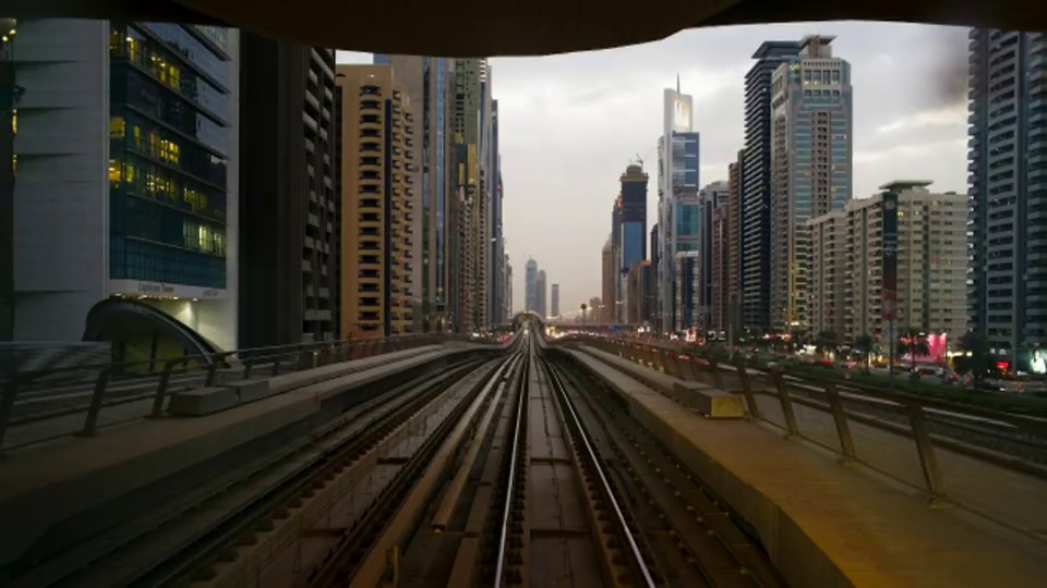 一辆地铁车辆在迪拜谢赫扎耶德公路旁的高架轨道地铁系统上行驶，穿过车站，经过摩天大楼和其他商业建筑。视频素材