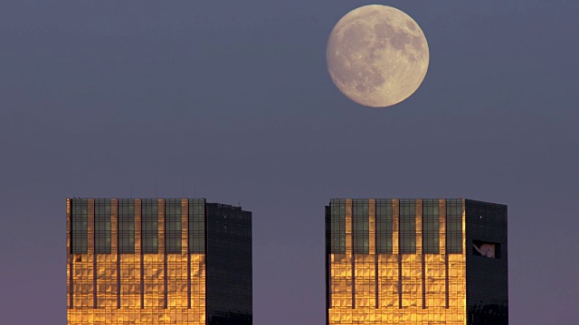 在纽约市晴朗的天空下，一轮满月从双子摩天大楼的顶端缓缓升起视频购买