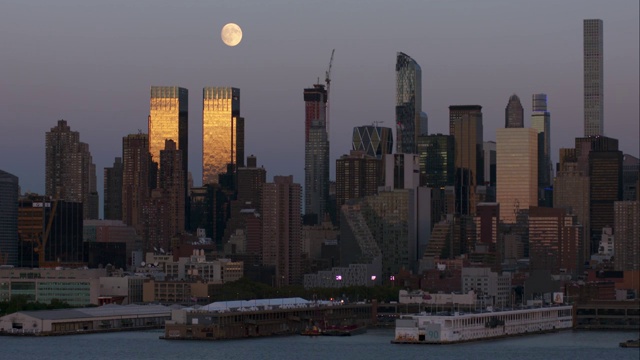 在一个晴朗的夜晚，纽约市上空的满月。两座建筑反映出与景色相反的温暖的天空。视频素材