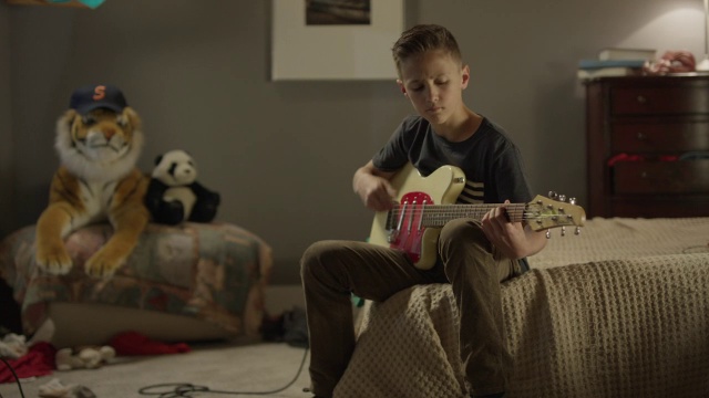 中等平移拍摄男孩在床上弹吉他/雪松山，犹他州，美国视频下载