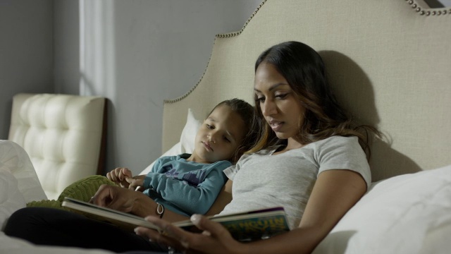 中等平移拍摄的母亲在床上看书给儿子/雪松山，犹他州，美国视频下载