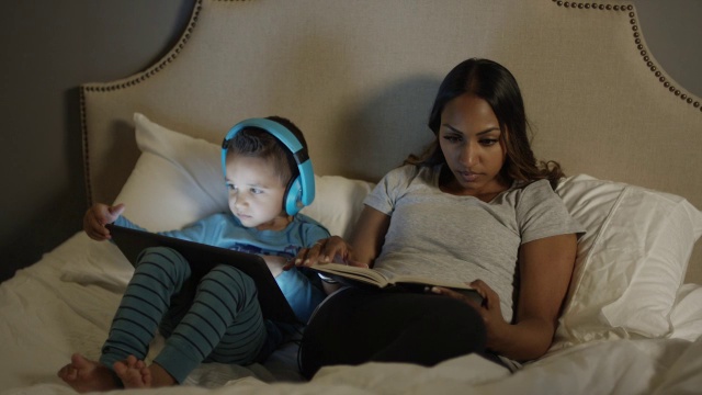 中等平移拍摄的母亲和儿子在床上看书和电子书/雪松山，犹他州，美国视频下载