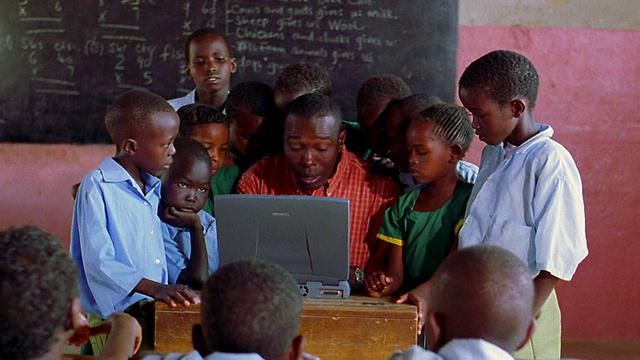 一名黑人男子坐在教室里使用电脑，孩子们围着他/肯尼亚视频素材