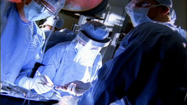 中镜头三名外科医生在手术室手术，助手在后台挂着设备视频素材