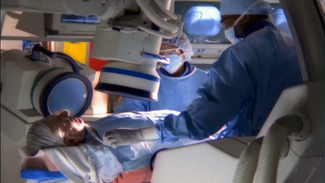 中焦镜头:男病人躺在心导管实验室，两个外科医生/一个拿着注射器点头视频素材