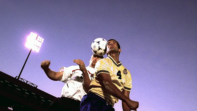 慢镜头低角广角拍摄两名足球运动员在对方的球队跳上足球在体育场视频素材