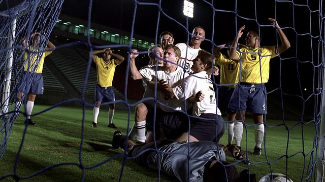 慢镜头远射足球运动员头球+进球，队友拥抱+欢呼在球场上视频素材