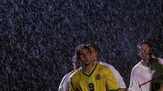 慢动作低角度MS足球运动员头球与对方球员在他周围的雨在晚上视频素材