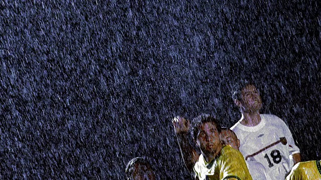 慢动作低角度MS足球运动员头球与对方球员在他周围的雨在晚上视频素材