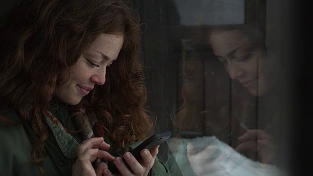 一个女人用手机发短信，手机的倒影映在窗户上视频素材