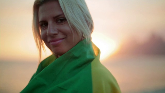 日落时分，伊帕内玛海滩上的女孩穿着巴西国旗摆姿势视频素材