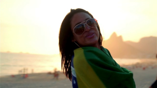 日落时分，伊帕内玛海滩上的女孩手举巴西国旗翩翩起舞视频素材
