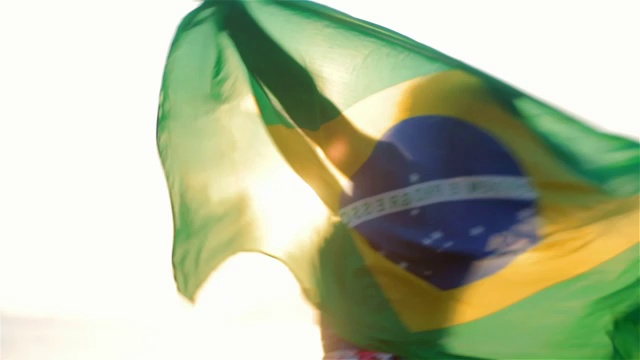 日落时分，伊帕内玛海滩上，女孩挥舞着巴西国旗旋转视频素材