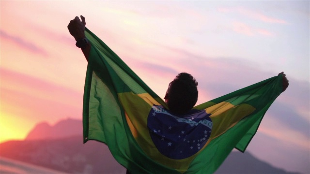 夕阳西下，伊波内玛海滩上，一个裹着巴西国旗的家伙挥舞着他的拳头，欢呼着视频素材