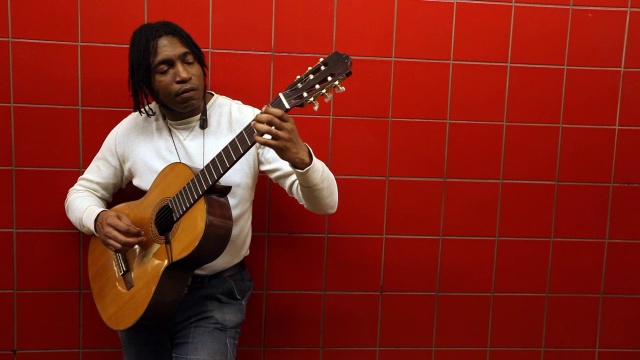 街头艺术家靠在红色瓷砖墙上，在城市地铁站弹原声吉他视频素材