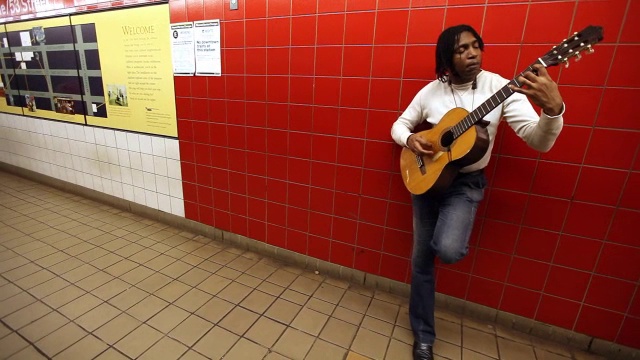 在纽约地铁里，一名男子靠在墙上弹着原声吉他寻求小费视频素材