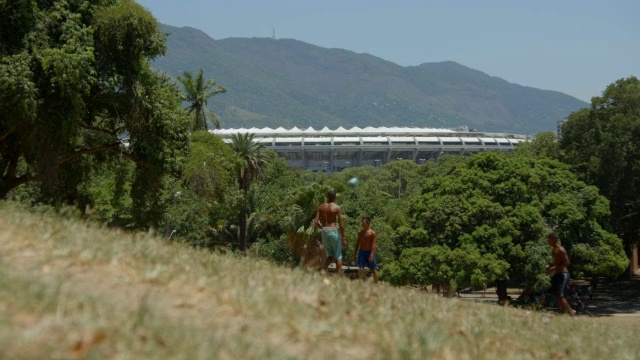 在俯瞰里约热内卢马拉卡纳体育场的山坡上，赤脚的巴西少年踢着足球，用头顶着足球视频素材