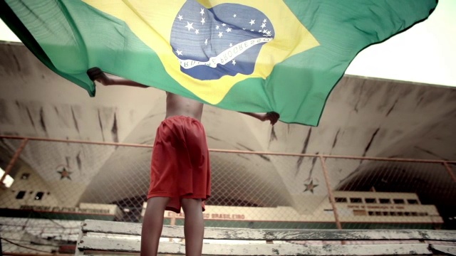 在慢镜头中，一个足球场上的小男孩将巴西国旗举过头顶视频素材