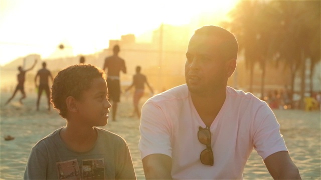 父亲和儿子在阳光明媚的巴西海滩上交谈视频素材