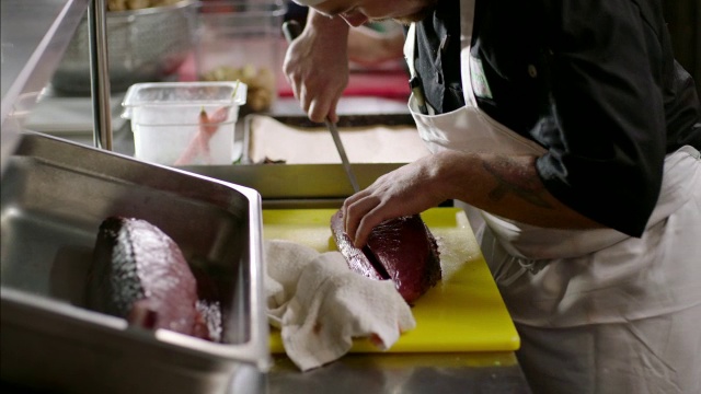 在繁忙的厨房餐厅，专业厨师在准备桌上切厚的金枪鱼牛排视频素材