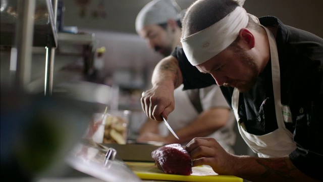 在繁忙的厨房餐厅里，厨师小心翼翼地将金枪鱼排切在砧板上视频下载