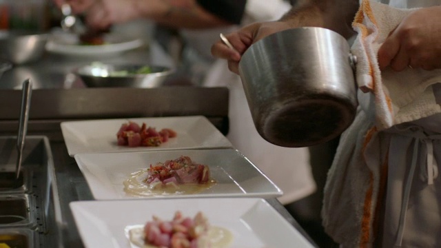 美食家在餐厅厨房用勺子把酱汁浇在热气腾腾的扇贝上视频素材