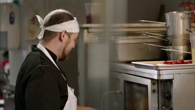 在餐厅厨房，主厨与厨房工作人员聊天，并将平底锅放入烤箱视频素材
