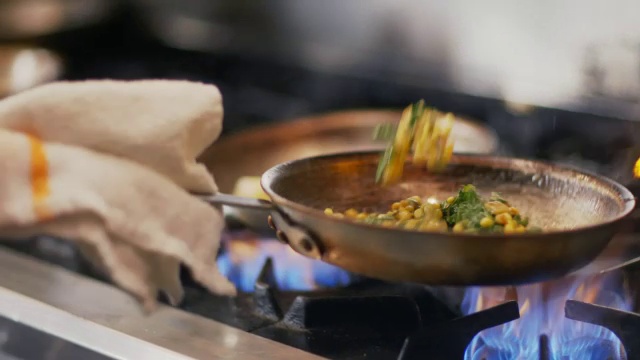 厨师将绿叶蔬菜加入玉米混合物中，在餐厅厨房的炉子上翻动煎锅视频下载