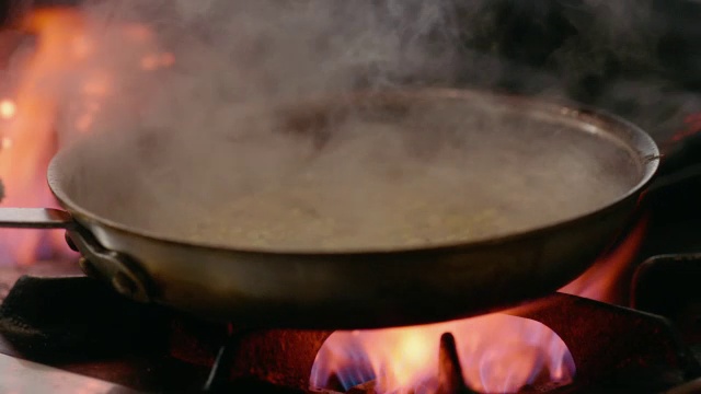 在餐厅的厨房里，厨师用铁锅在燃烧的炉子上慢动作地摇晃着玉米煮豆视频素材